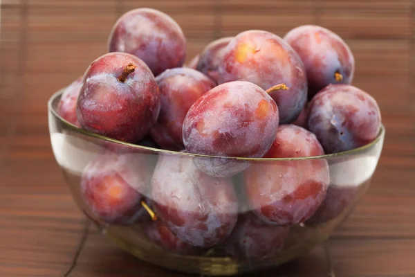 Plums in a glass bowl on a bamboo mat — Stock Photo, Image