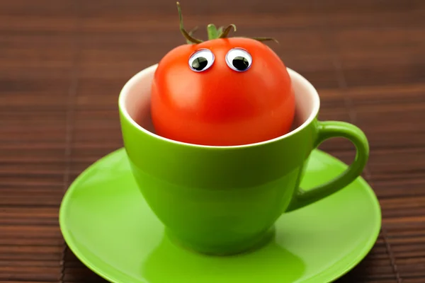 Tomate avec les yeux dans la tasse sur un tapis de bambou — Photo