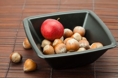 Hazelnuts in a bowl and apples on a bamboo mat