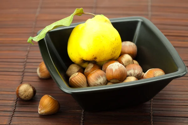 Hazelnuts in a bowl and quinces on a bamboo mat — Stock Photo, Image