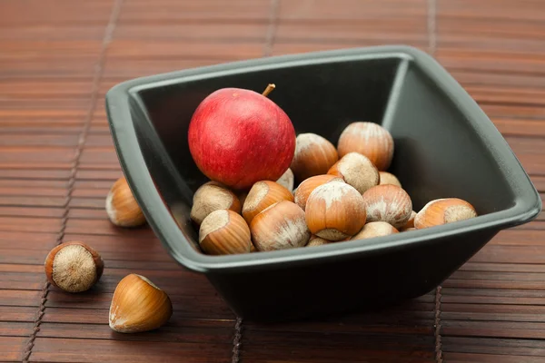 Noisettes dans un bol et pommes sur un tapis de bambou — Photo