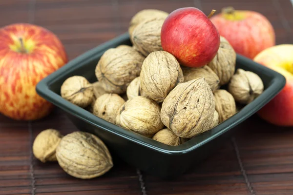 Walnuts and apples in a bowl on a bamboo mat — Stock Photo, Image