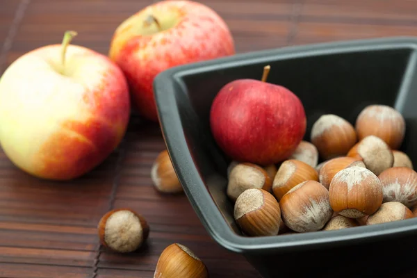 Hazelnuts in a bowl and apples on a bamboo mat — Stock Photo, Image