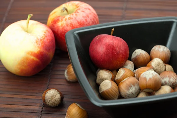 Hasselnötter i en skål och äpplen på en bambu matta — Stockfoto