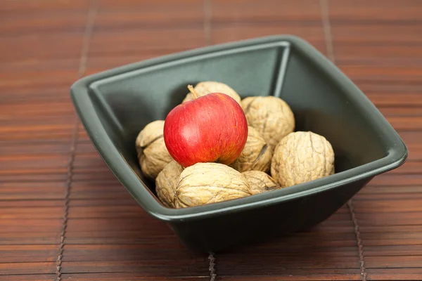 Walnuts and apples in a bowl on a bamboo mat — Stockfoto