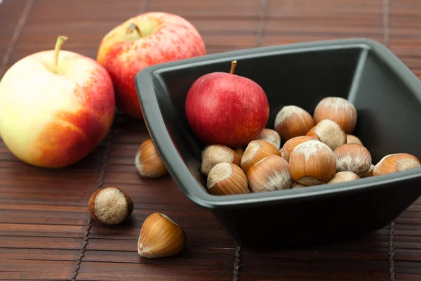 Avellanas en un tazón y manzanas en una estera de bambú —  Fotos de Stock