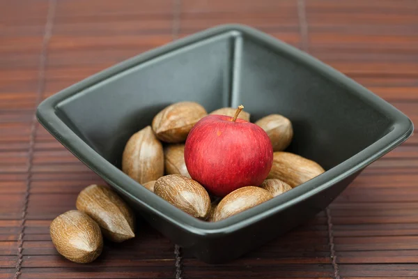 Pecans and apples in a bowl on a bamboo mat — Stock Photo, Image