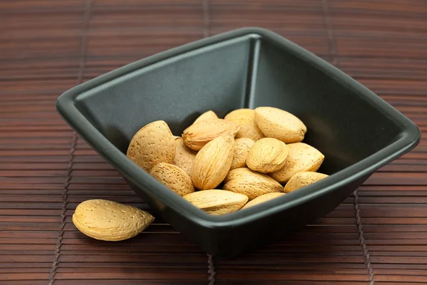 Almonds in a bowl on a bamboo mat — Stock Photo, Image