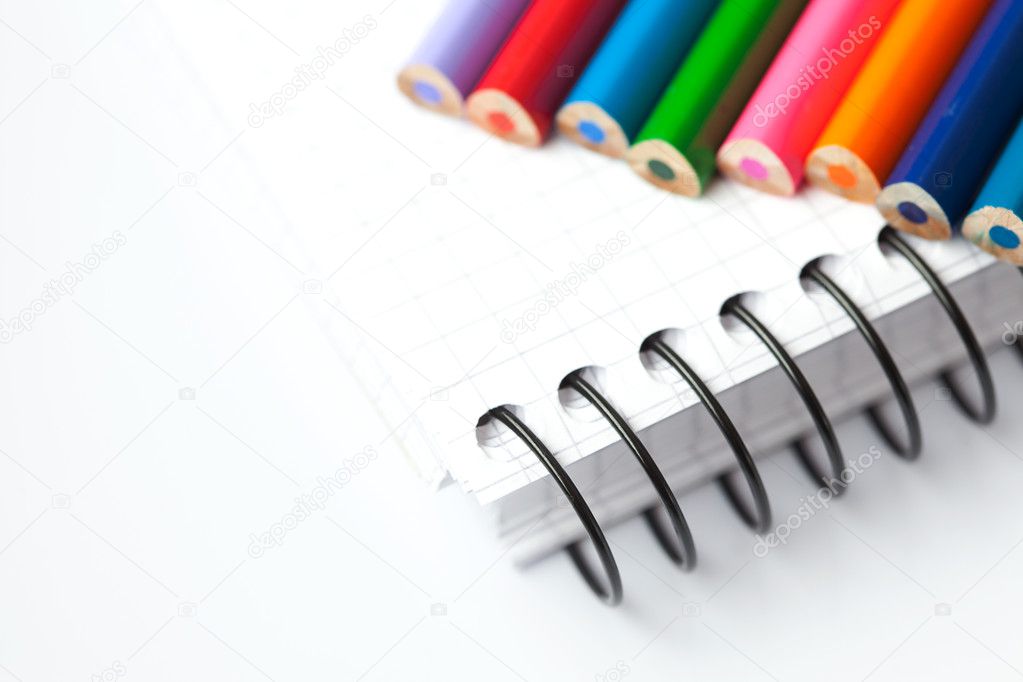 Colored pencils and a notebook isolated on white