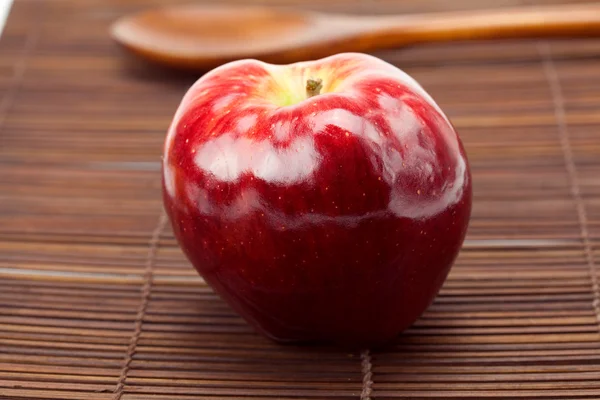 Red apple and a wooden spoon on a bamboo mat — Stock Photo, Image