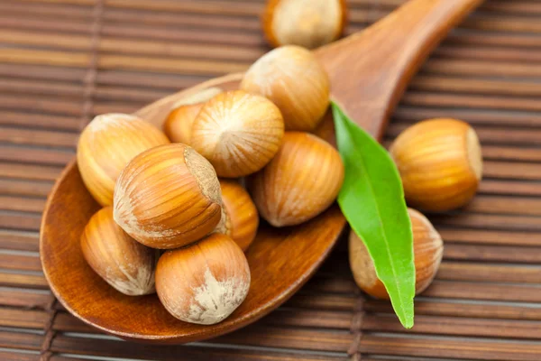 Hazelnuts and green leaf on a wooden spoon on a bamboo mat — Stock Photo, Image