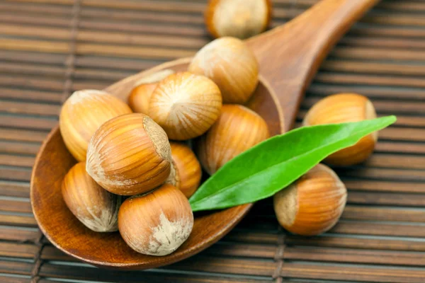Hazelnuts and green leaf on a wooden spoon on a bamboo mat — Stock Photo, Image