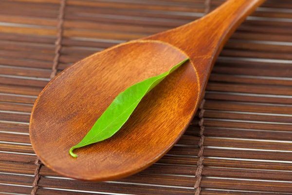 Folha verde na colher de madeira em um tapete de bambu — Fotografia de Stock