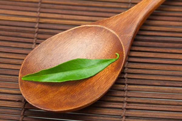 Green leaf on the wooden spoon on a bamboo mat — Stock Photo, Image