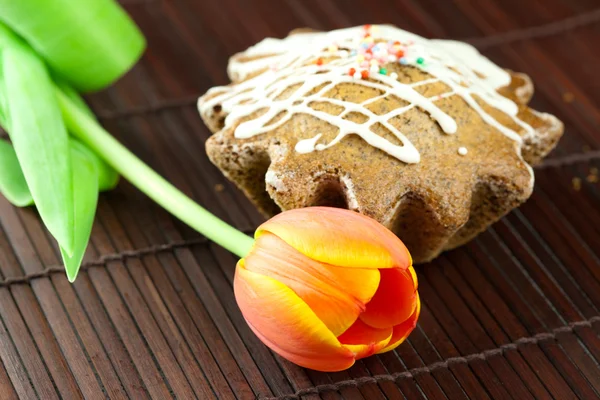 Kuchen mit Zuckerguss und einer auf einer Bambusmatte liegenden Tulpe — Stockfoto