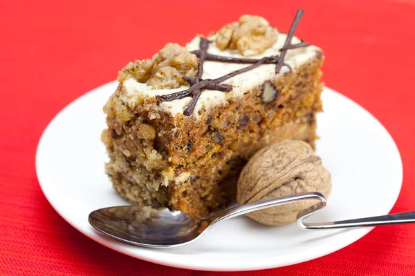 Piece of cake with nuts and spoon lying on a plate — Stock Photo, Image