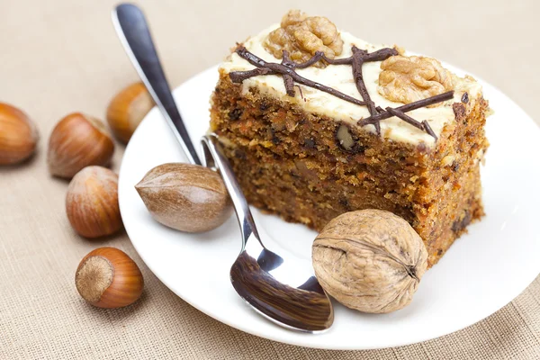 Piece of cake with nuts and spoon lying on a plate — Stock Photo, Image
