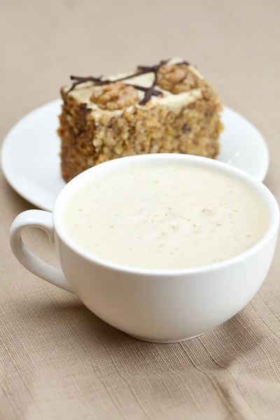 Tasse de cappuccino, un morceau de gâteau avec des noix couchées sur l'assiette — Photo
