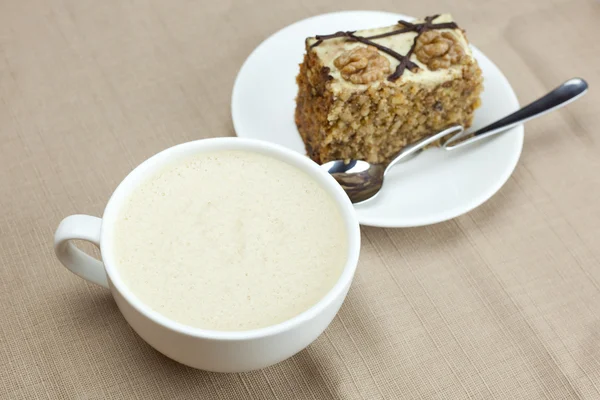 Чашка капучино, кусок торта с орехами и ложка лежа о — стоковое фото