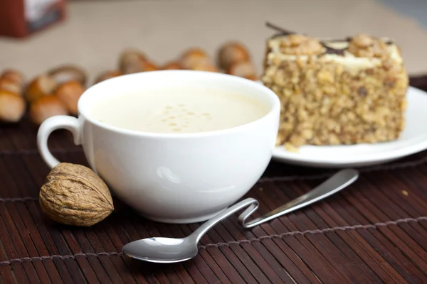Šálek cappuccino, hračka s ořechy na talíř, který leží na — Stock fotografie