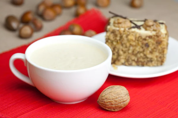 Cup of cappuccino, a piece of cake with nuts on a plate lying on — Stock Photo, Image