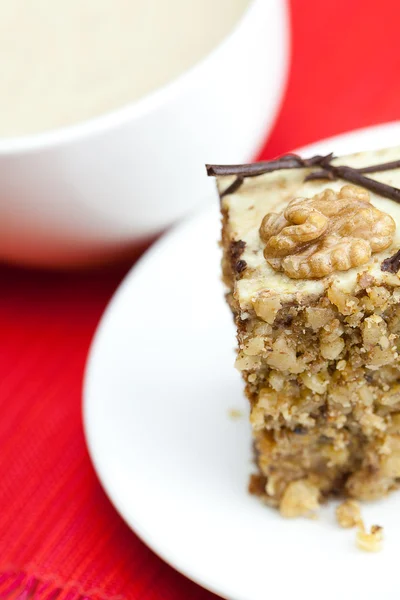 Cup of cappuccino, a piece of cake with nuts on a plate lying on — Stock Photo, Image