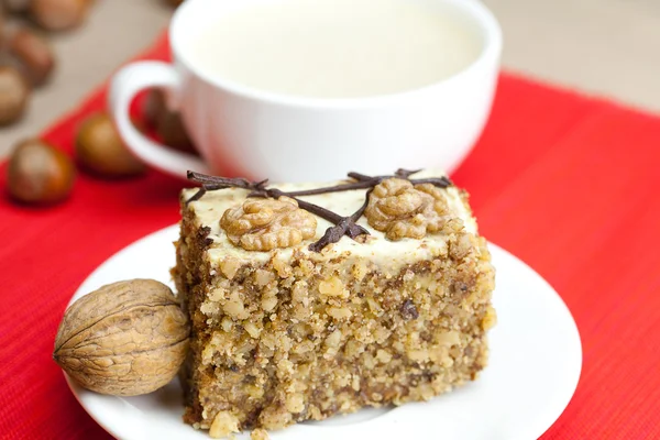 Coupe de cappuccino, un morceau de gâteau avec des noix sur une assiette couchée sur — Photo