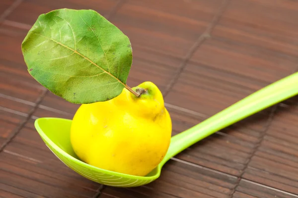 Mele cotogne gialle con una foglia verde in un cucchiaio su un tappetino di bambù — Foto Stock