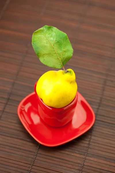 Membrillos amarillos con hojas verdes en una taza sobre una estera de bambú — Foto de Stock