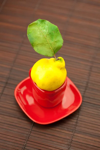 Yellow quinces with green leaves in a cup on a bamboo mat — Stock Photo, Image