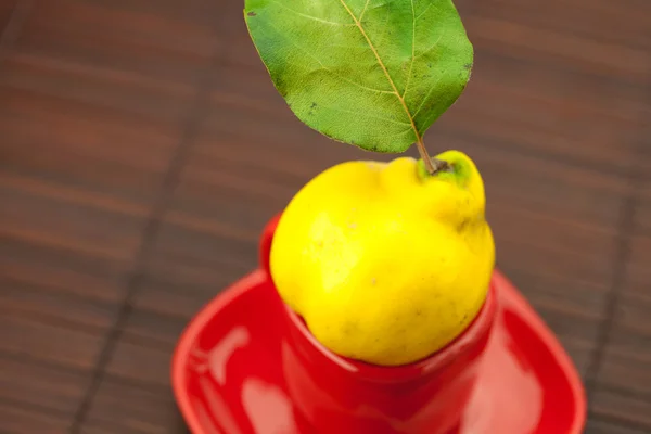 Yellow quinces with green leaves in a cup on a bamboo mat — Stock Photo, Image