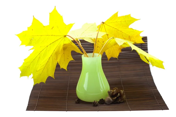 Hojas de arce amarillo y brotes en un jarrón en una estera de bambú —  Fotos de Stock