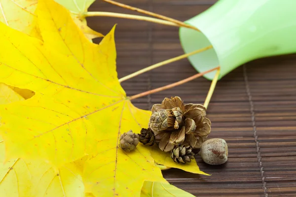 Gele esdoorn bladeren en toppen in een vaas op een bamboe-mat — Stockfoto