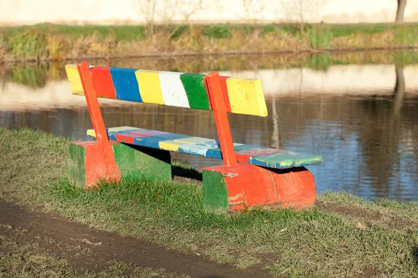 Flerfärgad bänken stående i en park nära dammen — Stockfoto