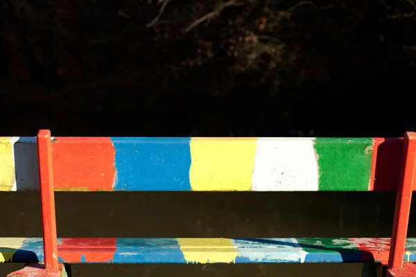 Разноцветная скамейка, стоящая в парке возле пруда — стоковое фото