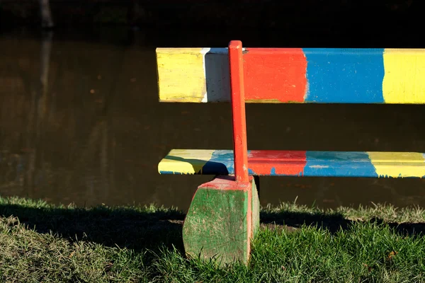 Flerfärgad bänken stående i en park nära dammen — Stockfoto