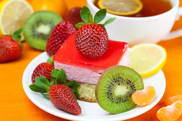 Thé au citron, kiwi, gâteau et fraises couchés sur le tissu orange — Photo