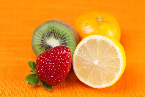 Kiwi, limón, mandarina y fresas que yacen sobre la tela naranja —  Fotos de Stock