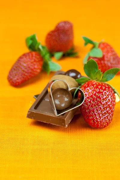 Chocolate bars, strawberry, heart and the candy on the orange fa — Stock Photo, Image
