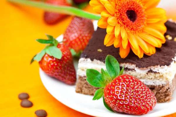 Gerbera, cake en aardbeien liggend op het oranje weefsel — Stockfoto