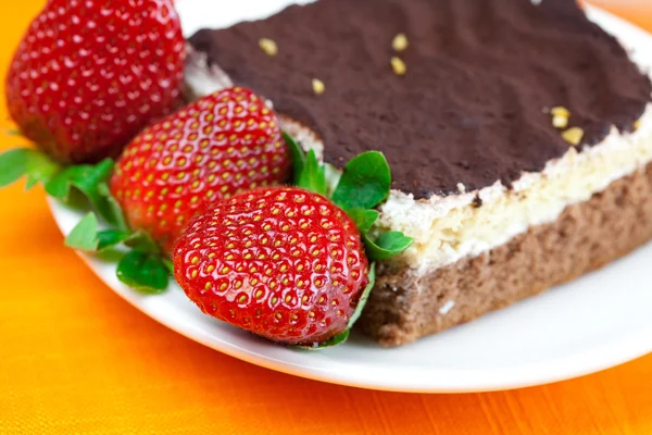 Gâteau sur une assiette et fraises couchées sur le tissu orange — Photo