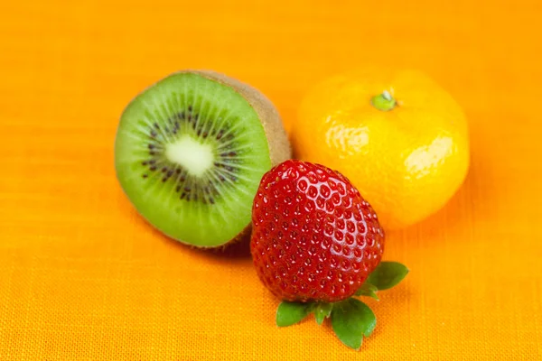 Kiwi, mandarin och jordgubbar liggande på orange tyg — Stockfoto
