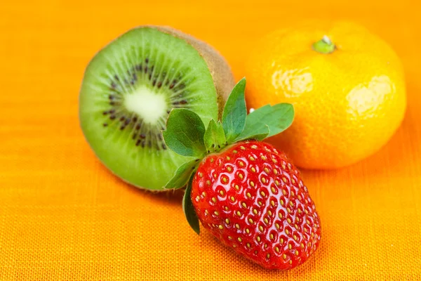 Kiwi, Mandarine und Erdbeeren liegen auf dem orangefarbenen Stoff — Stockfoto