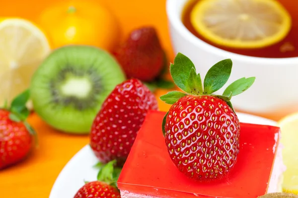 Citroenthee, kiwi, taart en aardbeien liggend op het oranje weefsel — Stockfoto