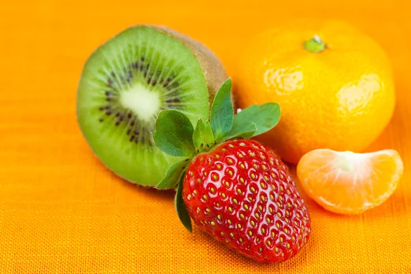 Kiwi, mandarine et fraises couchés sur le tissu orange — Photo
