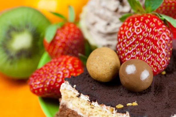Pastel, caramelos de chocolate, mandarina, kiwi y fresas en el o —  Fotos de Stock