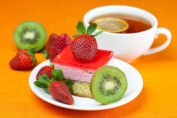 Chá de limão, kiwi, bolo e morangos deitados no tecido laranja — Fotografia de Stock