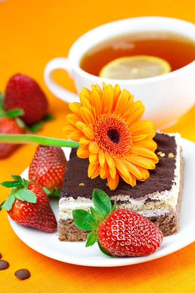 Gerbera, Zitronentee, Kuchen und Erdbeeren liegen auf dem orangefarbenen Tisch — Stockfoto