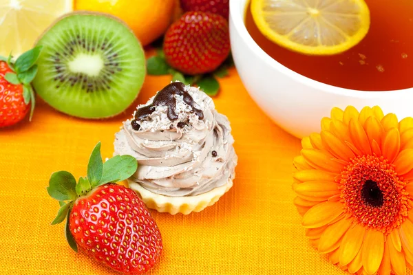 Gerbera, lemon tea, mandarin, kiwi, cake and strawberries lying on t — стоковое фото