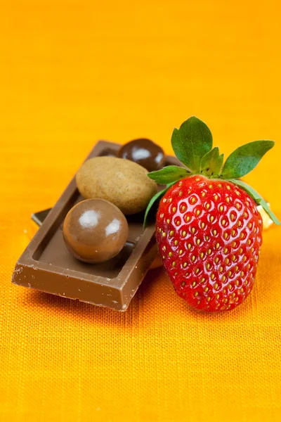Chocolate bars, strawberries and chocolates on the orange fabric — Stock Photo, Image